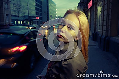 Pretty woman posing in pensive state of mind in the night street with blurred cars and streetlights on background, toned Stock Photo