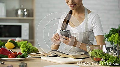 Pretty woman reading cooking book and calculating calories on smartphone app Stock Photo