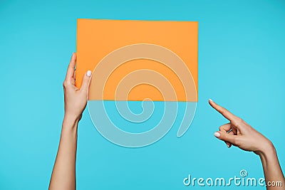 Pretty woman`s hand keeping orange paper in one hand and pointing on it with forefinger of another one, posing over blue Stock Photo