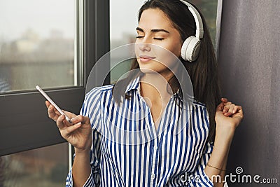 Pretty woman sitting by window and listening to relaxing music in headphones. Stream favorite songs directly from social networks Stock Photo