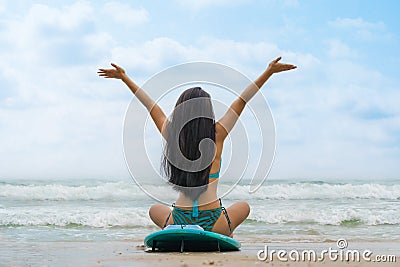 Woman surfer in bikini sitting on surfboard on beach in front of sea Stock Photo