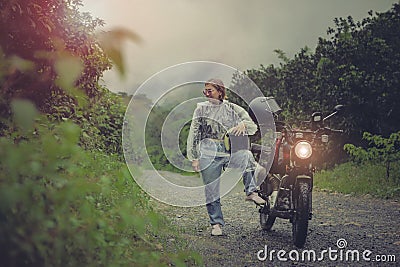 pretty woman wearing plastic rain clothes holding safety helmet standing beside small enduro motorcycle Stock Photo