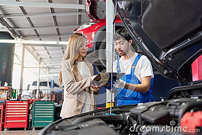 Pretty woman explain the problem of car to the professional vehicle maintenance man in uniform at garage. Car repair service Stock Photo