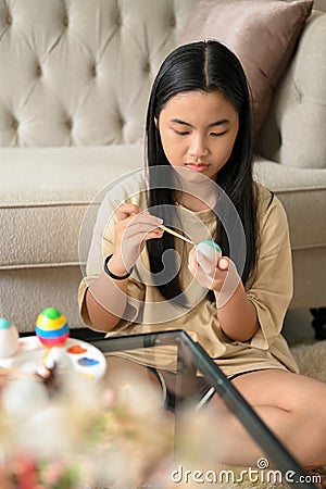 A pretty young Asian girl concentrates painting an Easter egg Stock Photo