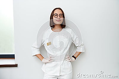 Pretty young doctor with closed eyes leaning against white wall in medical clinic. International doctors day Stock Photo