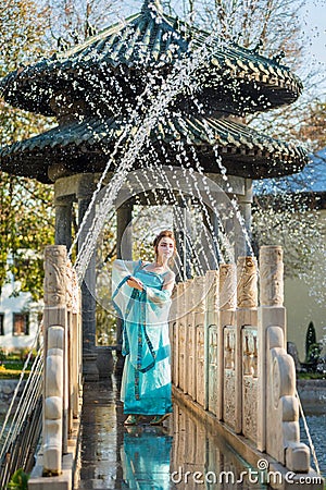 Pretty young geisha in water drops in blue dress standing near fountain Stock Photo