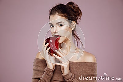 Pretty young girl biting red apple looking at camera over pink background. Stock Photo