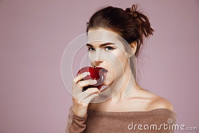 Pretty young girl biting red apple looking at camera over pink background. Stock Photo