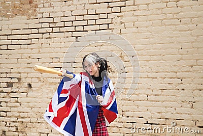 Pretty young girl in punk style threatening with a baseball bat. She carries the London flag on her shoulders Stock Photo