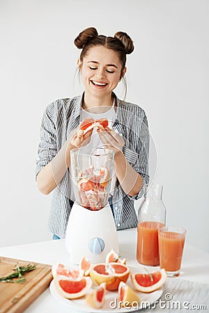 Pretty young girl smiling blending detox refreshing grapefruit smoothie over white wall. Healthy food concept. Stock Photo