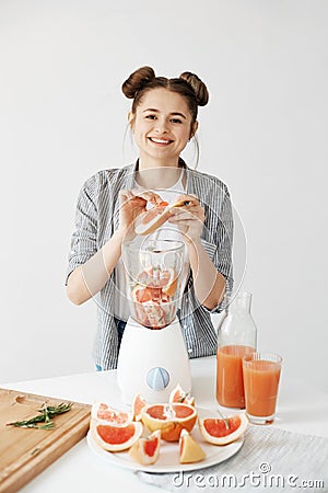 Pretty young girl smiling blending detox refreshing grapefruit smoothie over white wall. Healthy food concept. Stock Photo