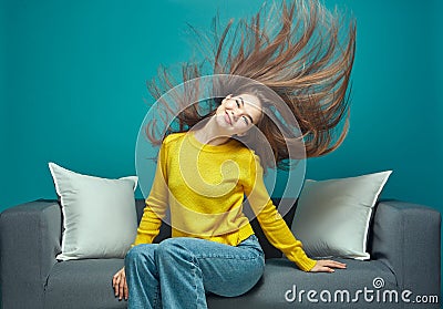 Pretty young girl with waving long hair shake head, having fun, sitting on sofa. Haircare cosmetics advertisement Stock Photo