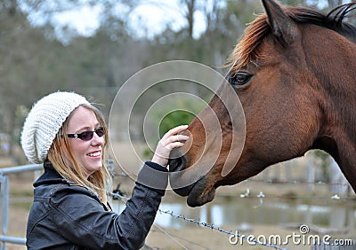 Pretty young happy woman outdoors with pet horse stroking him Stock Photo