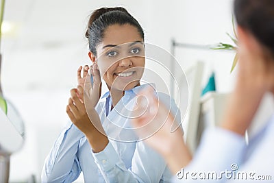 Pretty young lady putting on earrings in front mirror Stock Photo