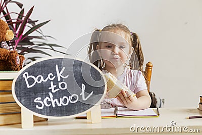 Pretty young schoolgirl eating sandwich at lunch break after classes. Back to school concept. Stock Photo