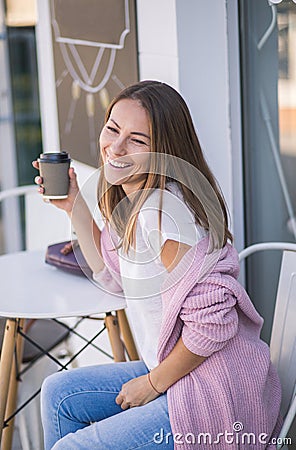 Pretty young stylish woman with paper cup of coffee to go sitting in sunny italian street cafe Stock Photo