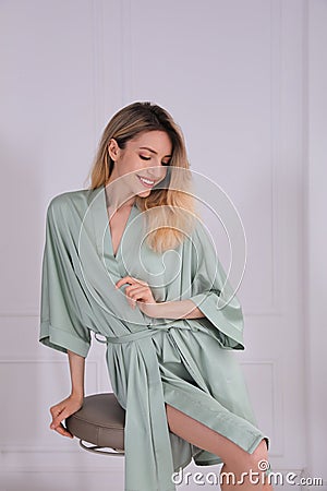 Pretty young woman in beautiful silk robe sitting on stool at home Stock Photo