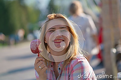 Pretty young woman eating and biting red caramel apple in the park in the sunny day Stock Photo