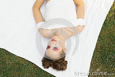 Young woman or girl with bright makeup and closed eyes is lying on a blanket on the lawn in the summer Stock Photo