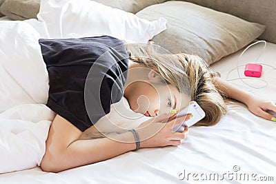 Pretty young woman lazy looking to phone while lying on bed Stock Photo