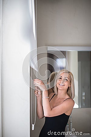 Pretty, young woman lowering the interior shades/blinds Stock Photo