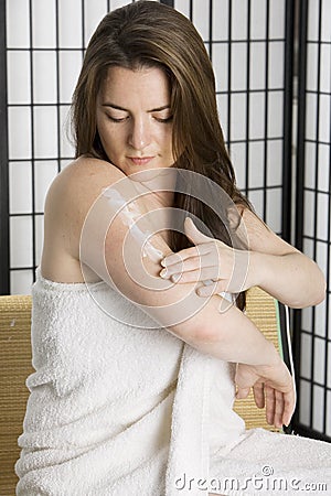 Pretty young woman puting on moisturizing lotion Stock Photo