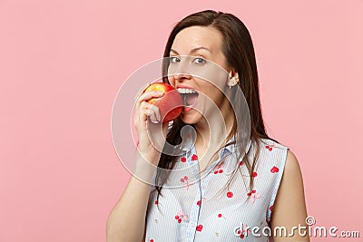 Pretty young woman in summer clothes hold biting fresh ripe red apple fruit on pink pastel wall background Stock Photo