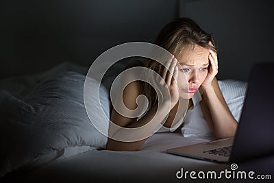 Pretty, young woman using her laptop computer in bed Stock Photo