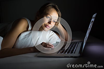 Pretty, young woman using her laptop computer in bed Stock Photo