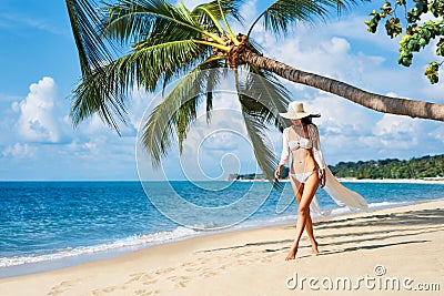 Pretty young woman in white bikini walking barefoot on the sea shore on tropical beach Stock Photo