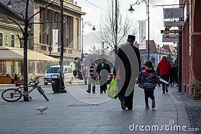 Priest dressed in black walking, holding a childs hand and carrying a bag with groceries Editorial Stock Photo