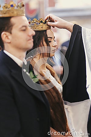 Priest putting on golden wedding crowns on bride and groom heads during holy matrimony in church Stock Photo