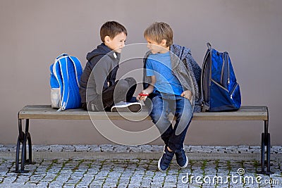 Primary education, school, friendship concept - two boys with backpacks sitting, talking and playing with spinner Stock Photo