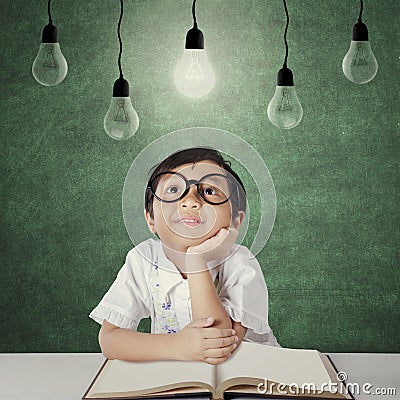 Primary school student sits under light bulb Stock Photo