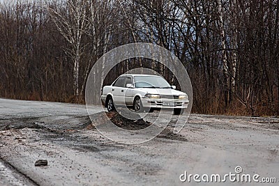 Primorsky Krai, Russia - 2016, autumn - A car drives along a bad, dead road among tall trees. Russian roads. Bad asphalt Editorial Stock Photo