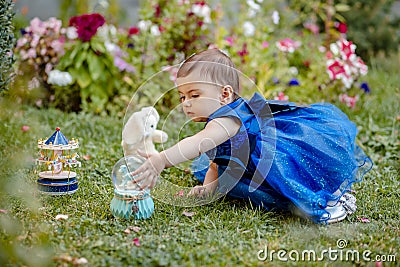 Princess baby girl sitting on grass in garden and playing with one of her toys Stock Photo