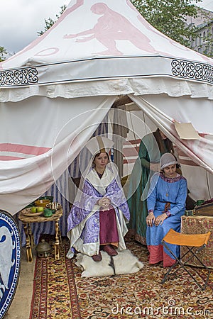 The princess and the maid in ancient historical dresses sit on the bright Turkish carpet in a white marquee. festival Vremena i Ep Editorial Stock Photo