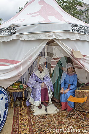 The princess and the maid in ancient historical dresses sit on the bright Turkish carpet in a white tent. festival Vremena i Epoh Editorial Stock Photo