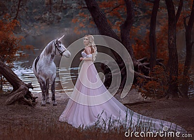 The princess met a unicorn in the forest. The blonde girl with a gentle make-up, is dressed in a long vintage dress with Stock Photo