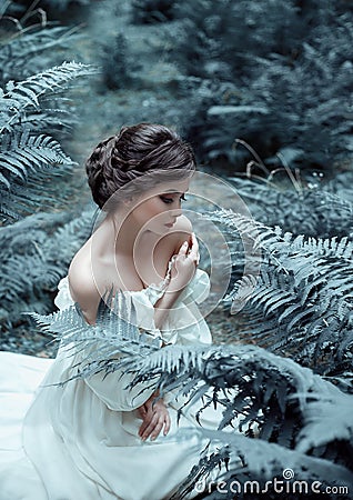 The princess sits on the ground in the forest, among the fern and moss. An unusual face. On the lady is a white vintage Stock Photo