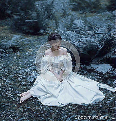 The princess sits on the ground in the forest, among the fern and moss. An unusual face. On the lady is a white vintage Stock Photo