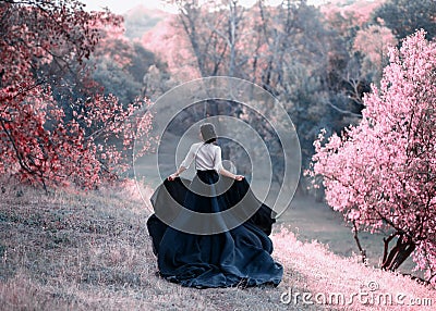 Princess in a vintage dress escapes. Walk through the picturesque autumn hills at sunset in pink tones. A long train of Stock Photo