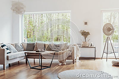 Print pattern pillows on a beige corner sofa by a big glass window in a warm living room interior with white walls Stock Photo