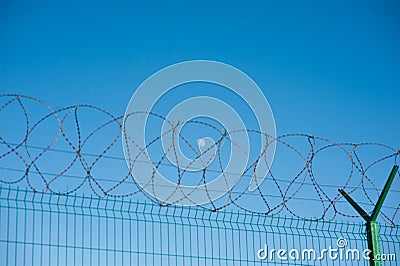 Prison concentration outdoor camp concept of barbed razor wire on fence with blue sky with moon on background Editorial Stock Photo