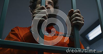 Prisoner in orange uniform and handcuffs holds metal bars Stock Photo