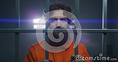 Prisoner stands in prison cell in handcuffs, looks at camera Stock Photo