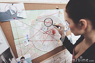 Private detective agency. Woman is looking at clue map with magnifying glass in office. Stock Photo