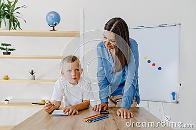 Attentive young woman tutor teacher helping little boy pupil with studying, correct mistakes explain learning material. Smiling Stock Photo