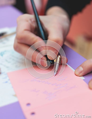 Process of calligraphy handwriting with an ink fountain pen feather, calligrapher practicing writing on a postcard paper using pen Stock Photo