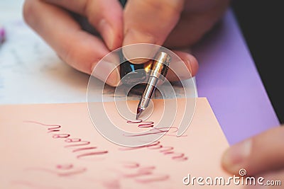 Process of calligraphy handwriting with an ink fountain pen feather, calligrapher practicing writing on a postcard paper using pen Stock Photo
